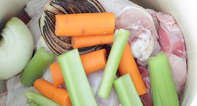 adding vegetables to a stockpot with chicken and meat