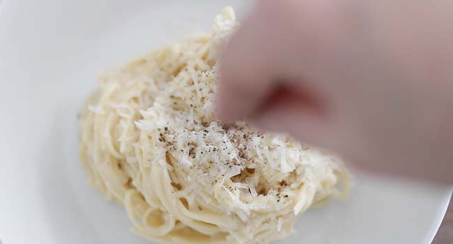garnishing spaghetti cacio e pepe with pecorino cheese