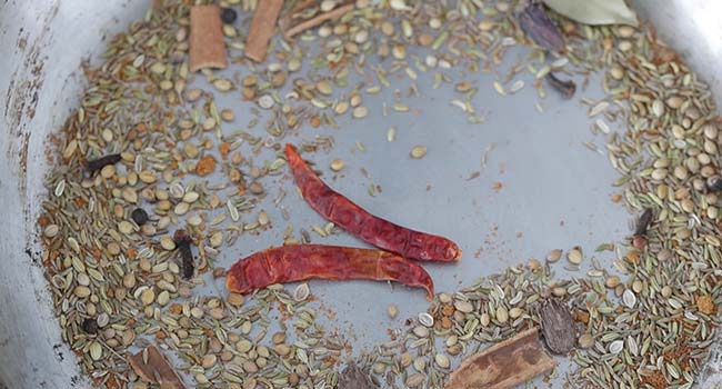 adding dried peppers to a chana masala powder