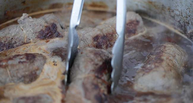 adding seared beef into a braising pan with beef stock