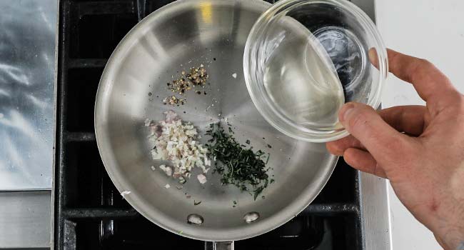 adding vinegar to a pan with herbs and shallots
