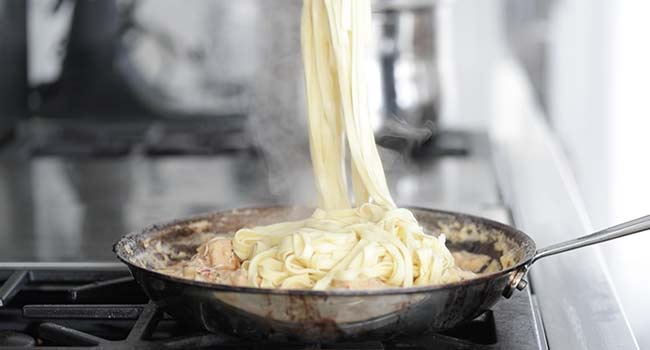tossing pasta in a creamy shrimp pasta