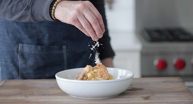 garnishing a cajun shrimp pasta with parmesan