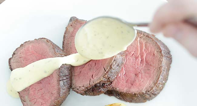 pouring bearnaise sauce onto beef tenderloin slices