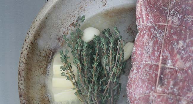 thyme and garlic in a pan with beef tenderloin