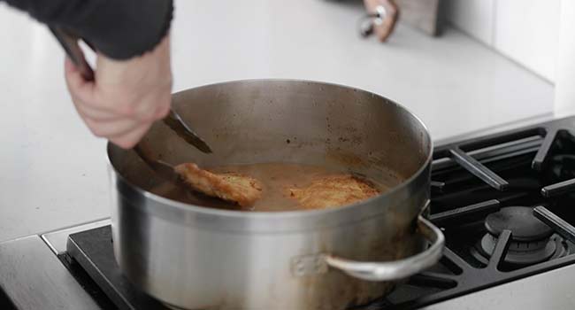 placing cooking battered chicken into a pan with thick stock