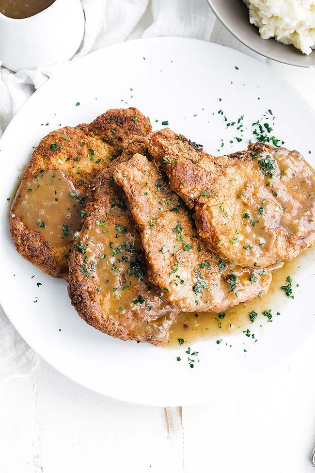 fried pork chops on a plate with parsley and gravy