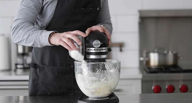 adding powdered sugar to a mixer with cream cheese