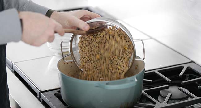 adding lentils to a pot with vegetables