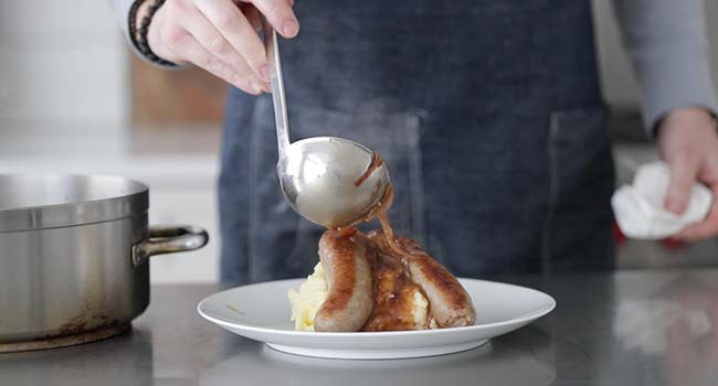 pouring onion gravy over bangers and mash