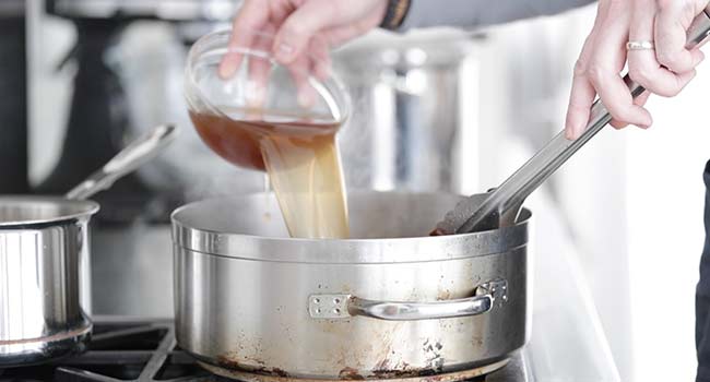 adding beef stock to a pot