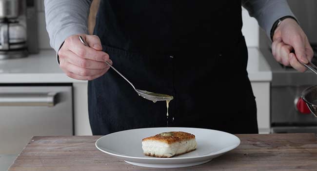 pouring a lemon butter sauce over halibut