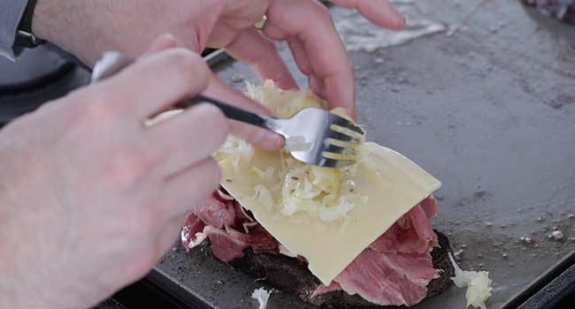 adding cheese and sauerkraut to a reuben sandwich