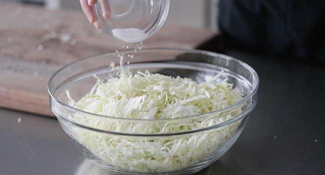 adding salt to a bowl of cabbage