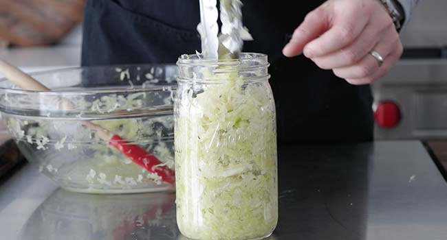 placing broken down cabbage into a mason jar