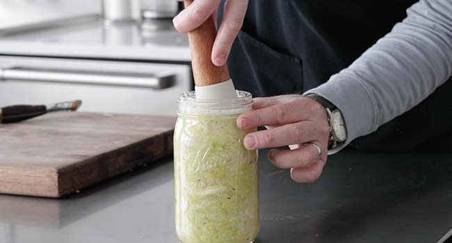 mashing down sauerkraut in a jar