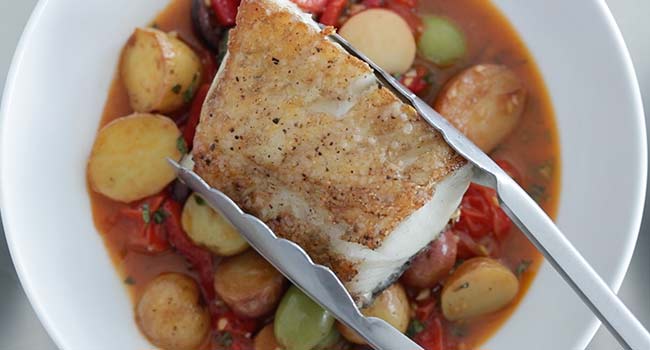 adding cooked sea bass to mediterranean ingredients