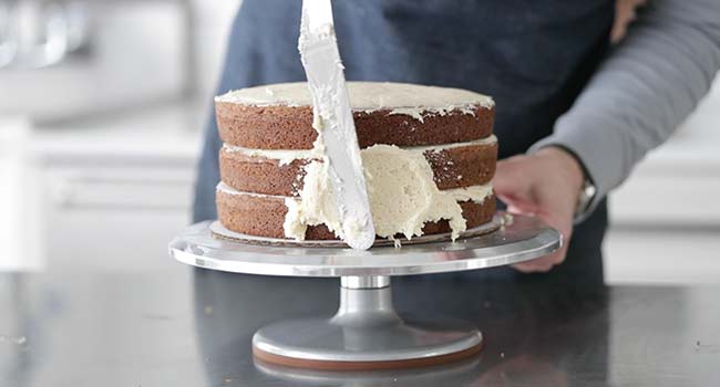 spreading cream cheese frosting onto a 3 layer carrot cake