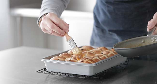 brushing hot cross buns with apricot jam