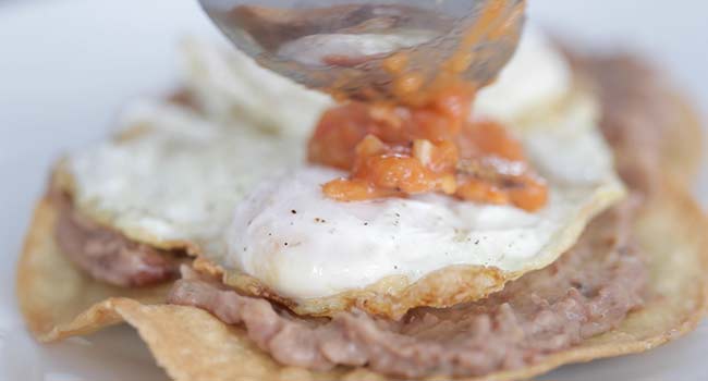 adding salsa on to a huevos rancheros