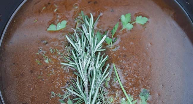 adding herbs and beef stock to a pot