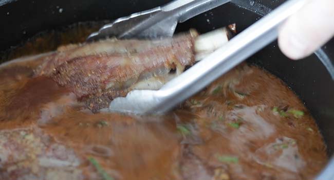 adding seared lamb shanks to a pot with herbs and beef stock