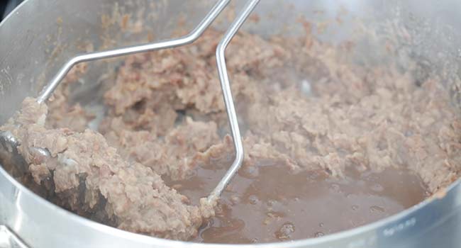 mashing cooked beans to make refried beans