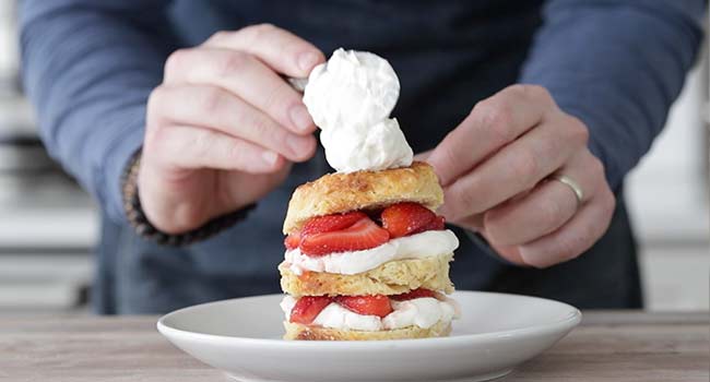 putting whipped cream on a strawberry shortcake