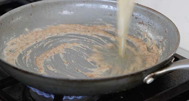 adding chicken stock to a pan with roux