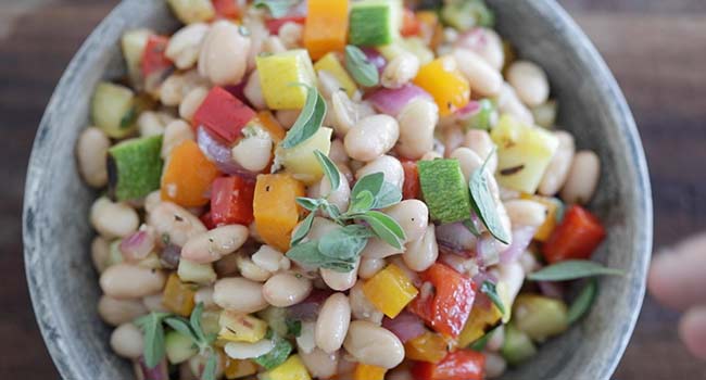 adding herbs to a mediterranean bean salad