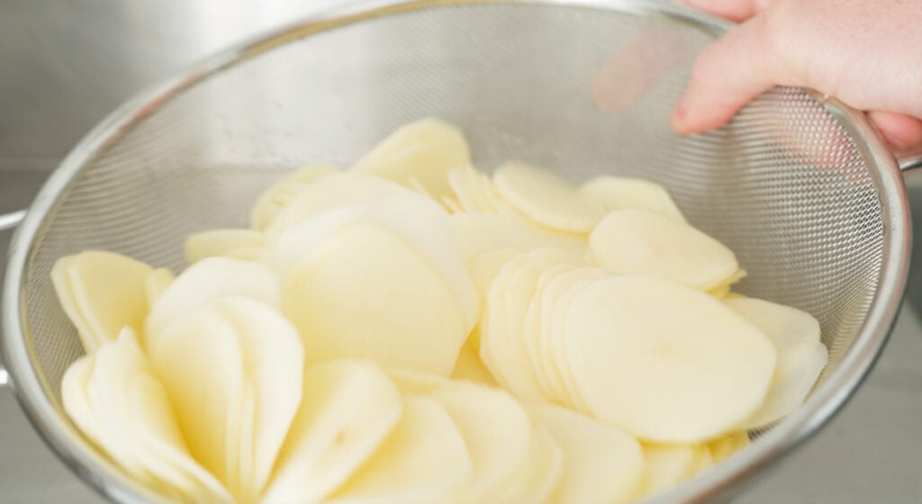 sliced potatoes in a mesh strainer