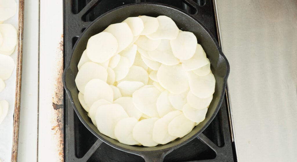 Skillet wiht another layer of sliced potatoes added