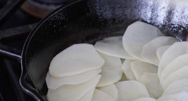 layering sliced potatoes in a pan