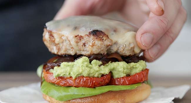 adding a turkey burger to a bun with lettuce, tomato, and onion