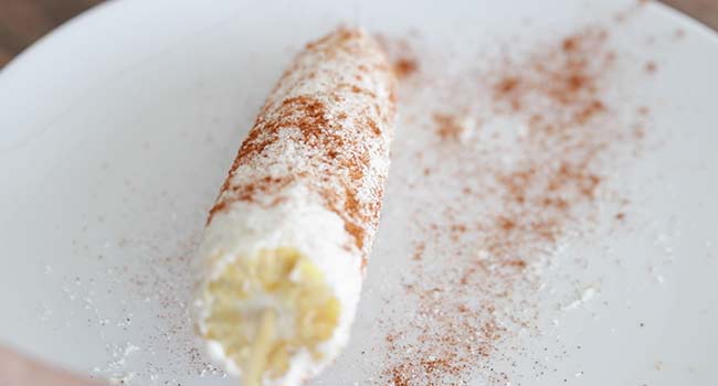 sprinkling chili powder on elotes