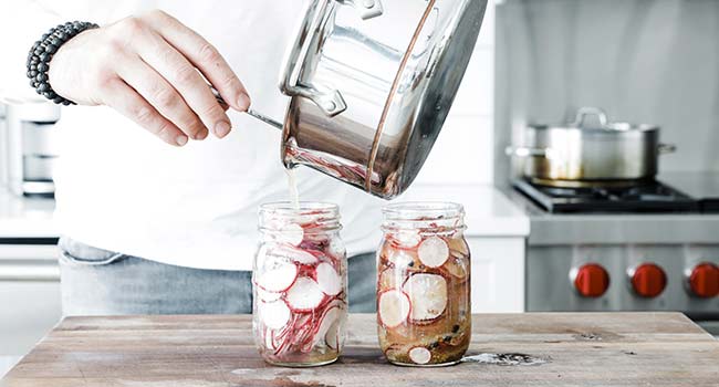 adding pickling liquid to a jar of sliced radishes