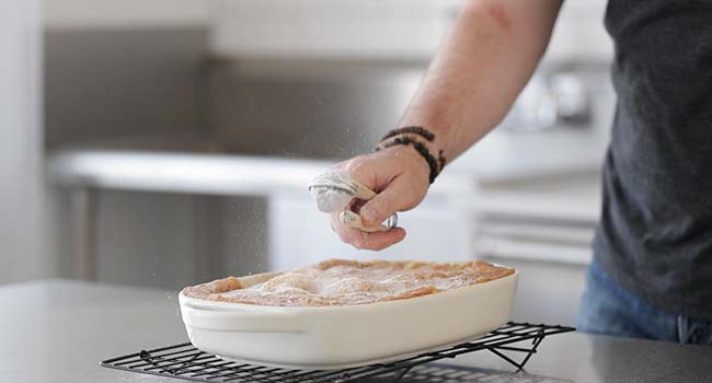 sprinkling ooey gooey butter cake with powdered sugar