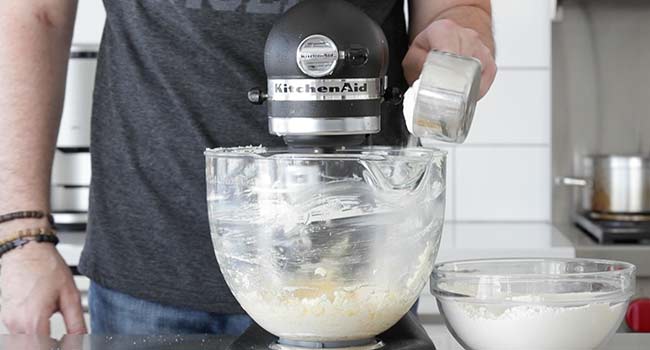 adding dry ingredients to a mixer with whipped butter