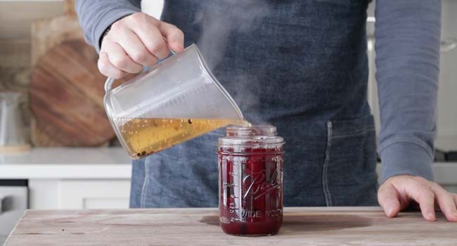 pouring a brine over cooked beets in a jar