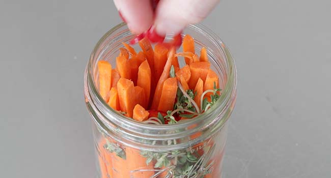 adding peppers to a jar with carrots