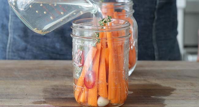 pouring hot brine over a jar of carrots