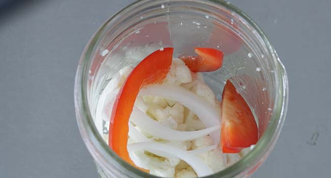 adding onions and bell peppers to a jar with cauliflower