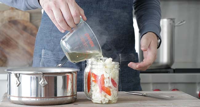 pouring a brine over top of a jar of cauliflower