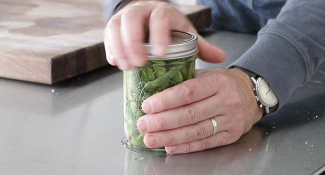 screwing on a lid to a jar of pickled green beans