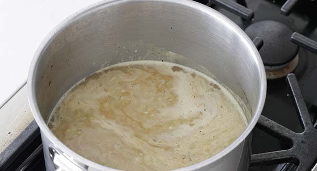 adding chicken stock to a pot