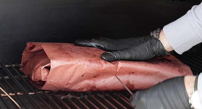 adding a wrapped brisket to the smoker