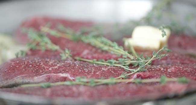 adding butter and herbs to a pan with steaks