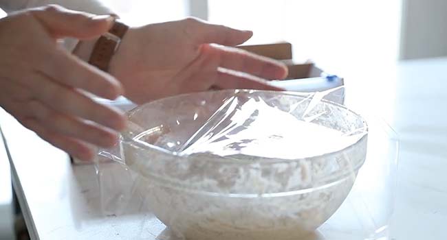 covering a bowl of pizza dough with plastic wrap