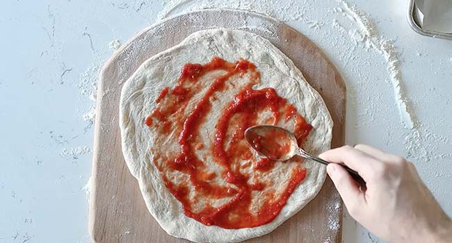spreading pizza sauce onto a pizza