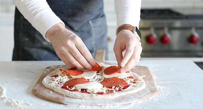 adding pepperoni to a pizza